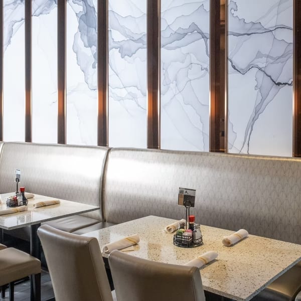 Restaurant interior with light-colored booths, granite tables, and a modern wall with abstract gray patterns.