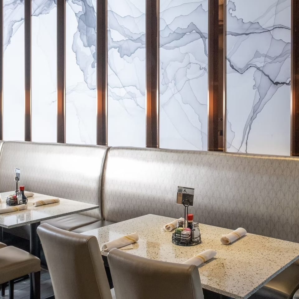 Restaurant interior with light-colored booths, granite tables, and a modern wall with abstract gray patterns.