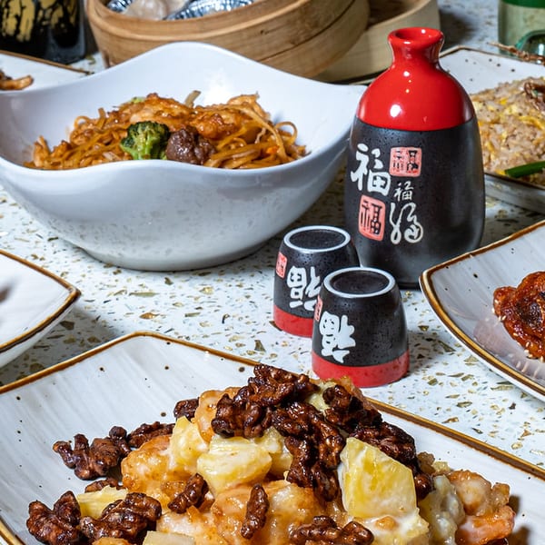 A vibrant spread of Asian dishes including noodles, fried rice, wontons, chicken, and shrimp with sake.