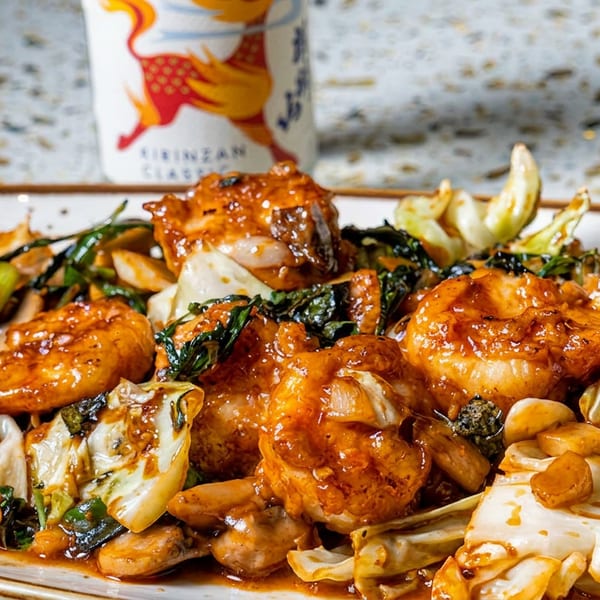 Plate of glazed shrimp stir-fried with cabbage, leafy greens, and garlic in a rich sauce.