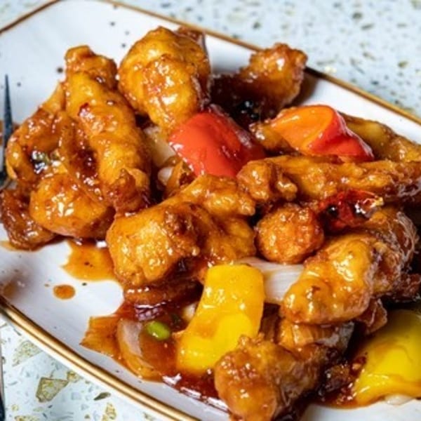 Sweet and sour chicken with bell peppers and onions on a white rectangular plate with a fork.