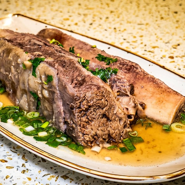 Braised beef ribs served with a savory broth and fresh green onions on a rectangular plate.