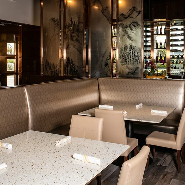 Modern restaurant dining area with beige booths, white tables, artistic dividers, and a well-stocked bar.