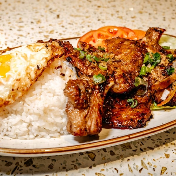 Grilled pork chops with rice, fried egg, tomatoes, and green onions on a speckled plate.