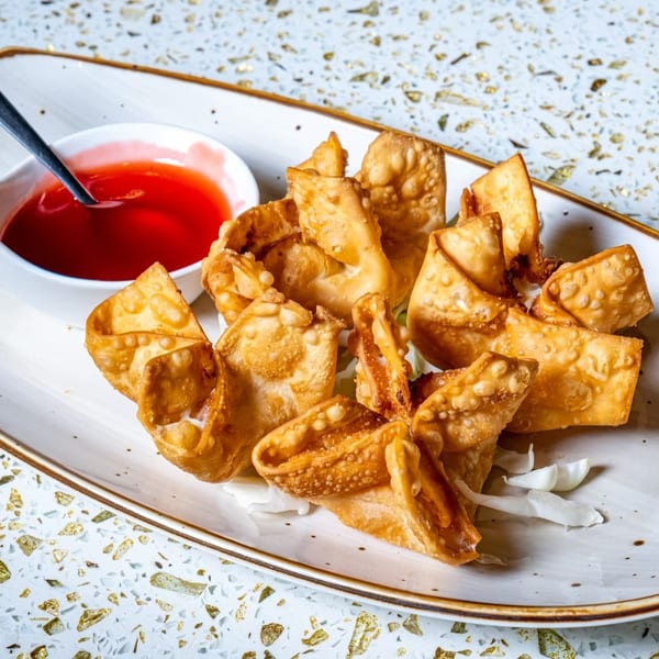 Crispy golden crab rangoon appetizers with a side of sweet and sour dipping sauce.