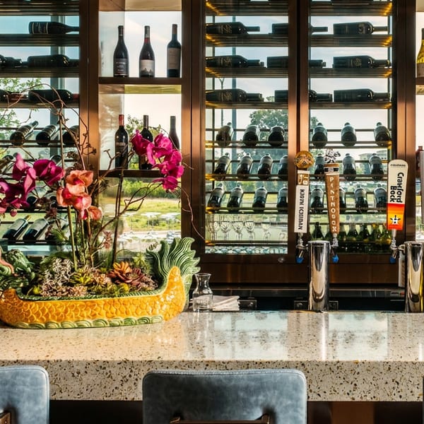 Modern bar with granite counter, blue stools, wine display, beer taps, and floral centerpiece.