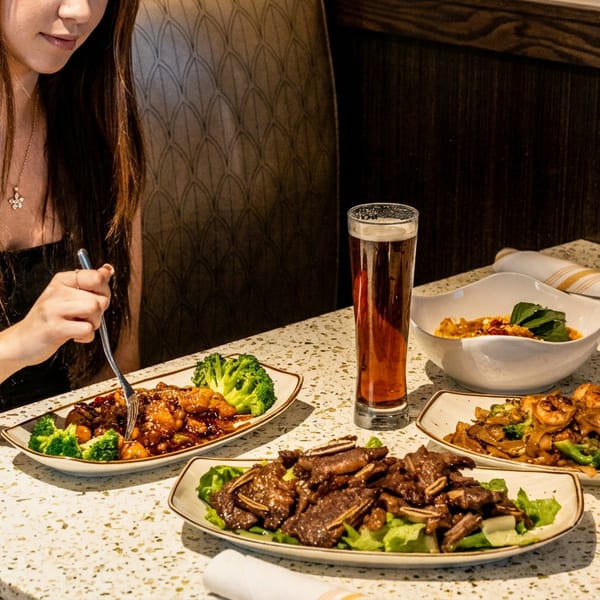 Woman enjoying several Asian dishes and a beer at a restaurant booth.