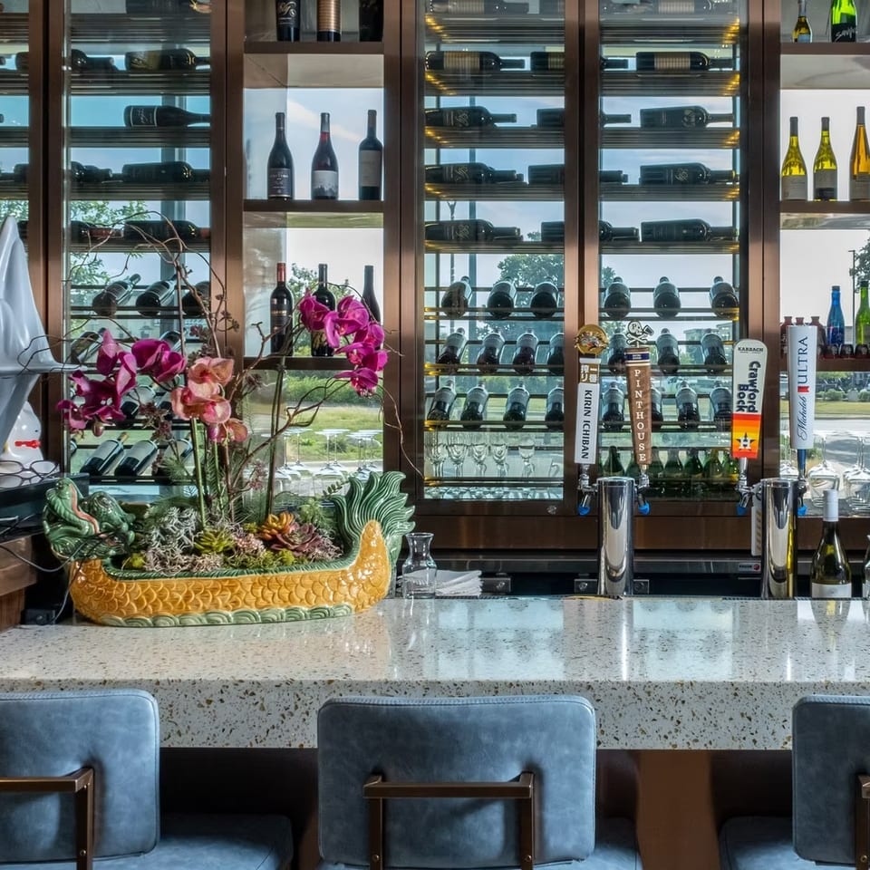Modern bar with a speckled countertop, blue stools, beer taps, and a wine display wall.